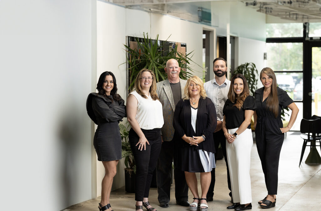 A team of seven photographed together in their Denver office by DHC Media.