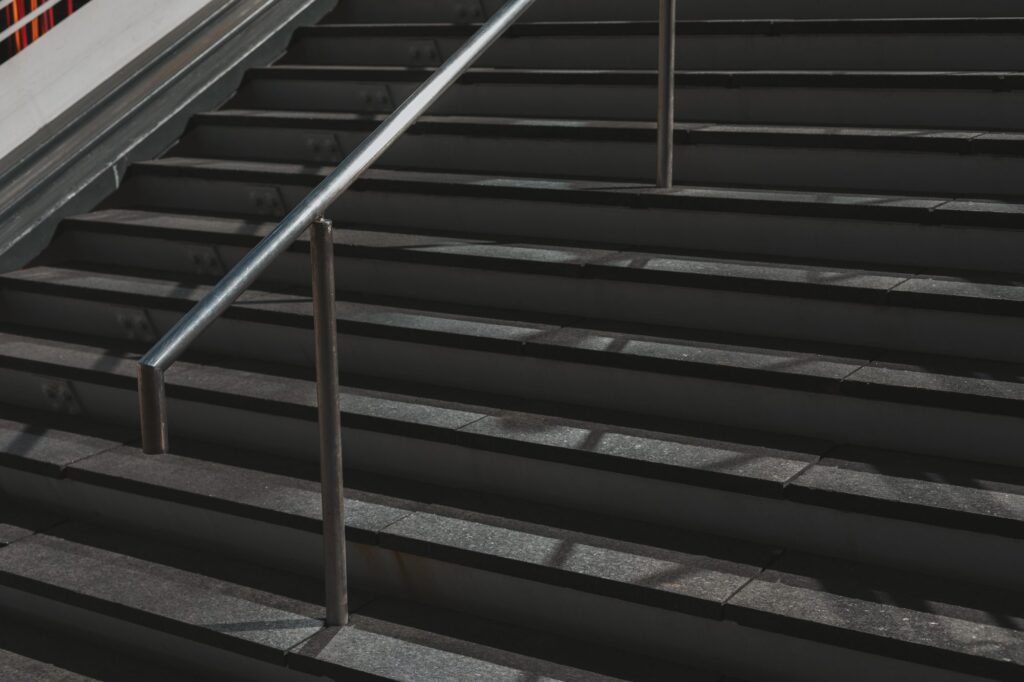 A metal handrail runs alongside a set of dark stone stairs in sunlight, casting branded shadows on the steps—subtle yet strong, much like a company's brand presence.