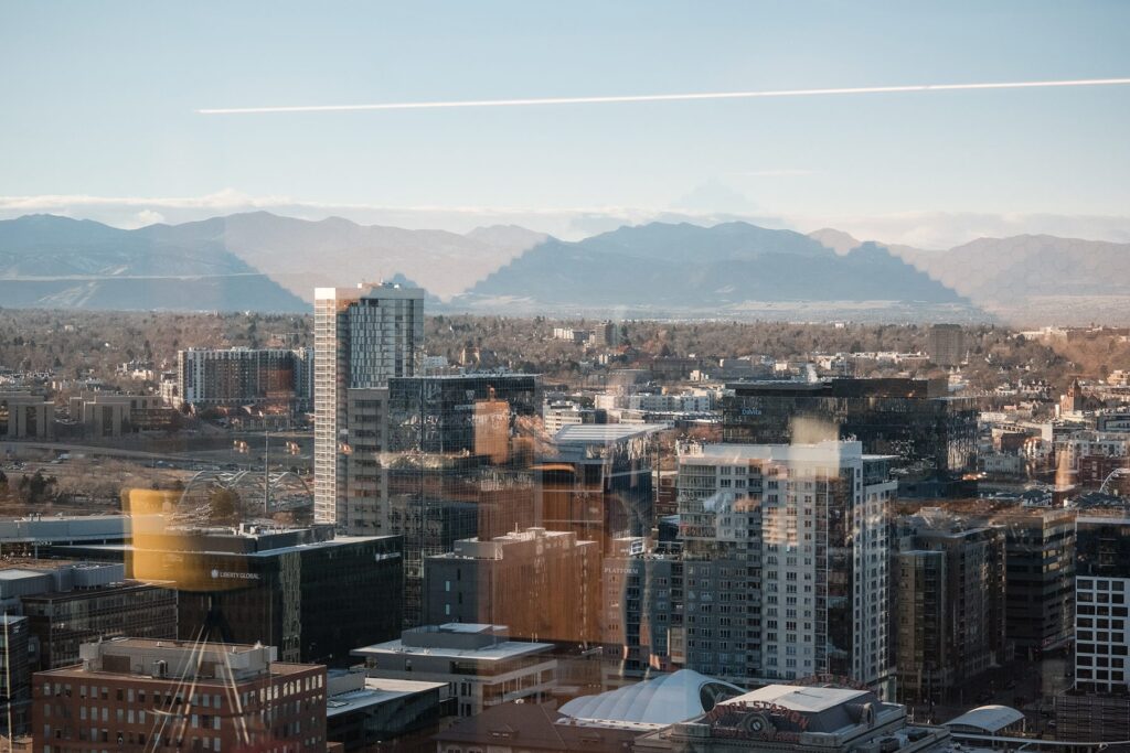 View of a cityscape with high-rise buildings and mountains in the background, seen through a window that reflects interior office furniture—perfect for those focused on building their brand presence or enhancing brand SEO.