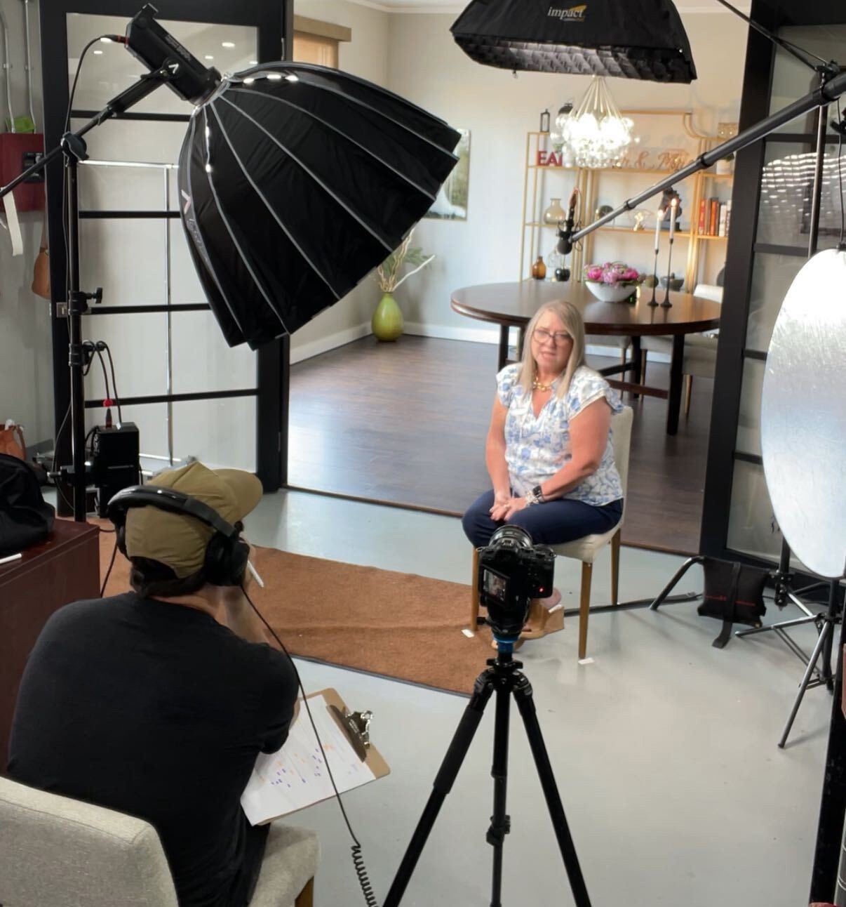 A DHC Media crew filming an interview on a lit set with softboxes and a camera on a tripod.